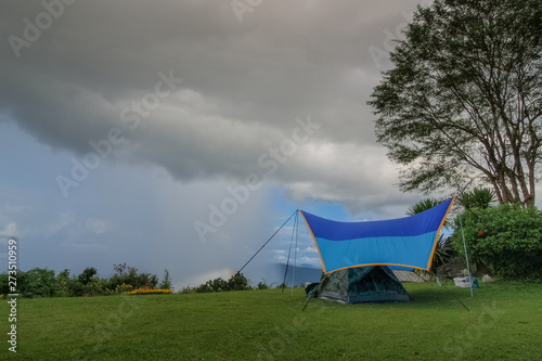 view of camping tent on green grass with rain storm and cloudy sky background, Pha Chu Camp Site, Sri Nan National Park, Nan, Thailand.