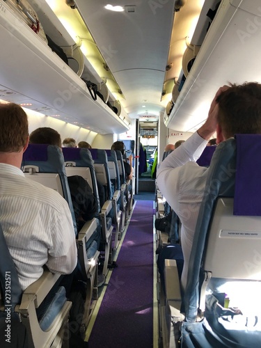 Interior of airplane with passengers on seats waiting for take off with door to the cockpit still open