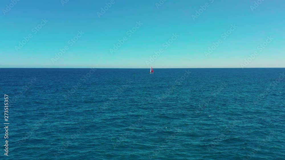 Aerial view. Beautiful sailing yacht with a red sail is sailing on the emerald sea on a sunny day. Aerial view. Beautiful sailing yacht with a red sail is sailing on the emerald sea on a sunny day.