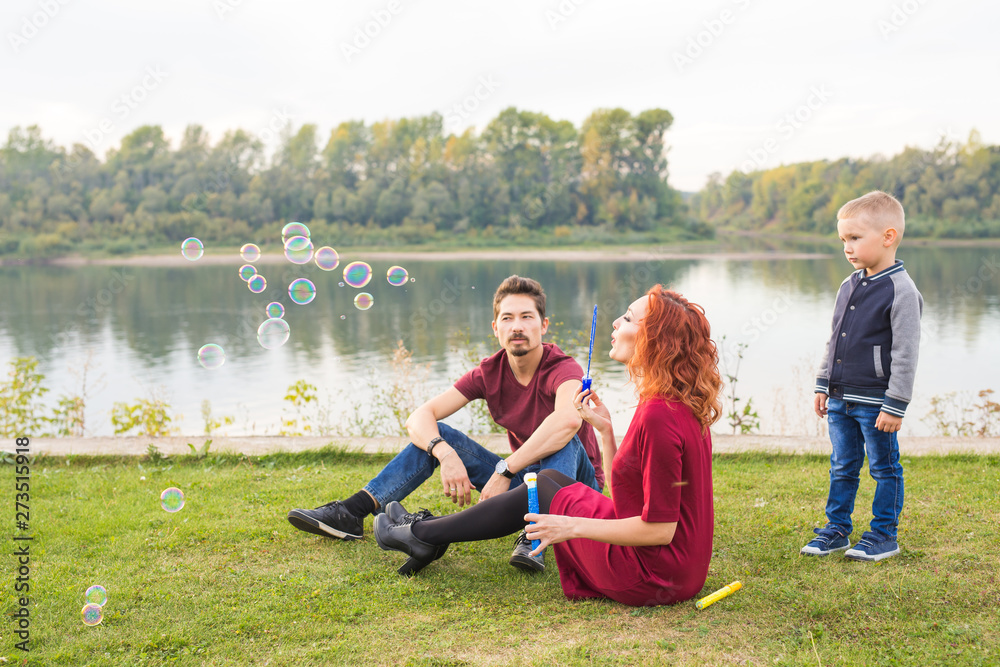 Family and nature concept - Mother, father and their child playing with colorful soap bubbles Family and nature concept - Mother, father and their child playing with colorful soap bubbles