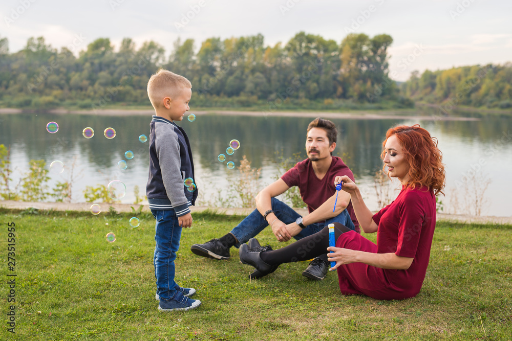 Family and nature concept - Mother, father and their child playing with colorful soap bubbles Family and nature concept - Mother, father and their child playing with colorful soap bubbles