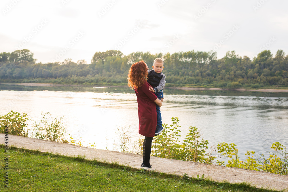 Motherhood and children concept - young mother with son in her arms near the river