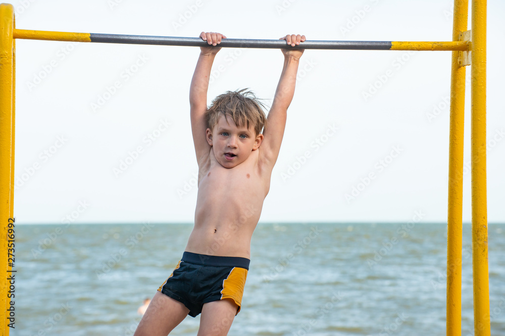 The boy on the bar performs the exercises, a strong and muscular athlete.