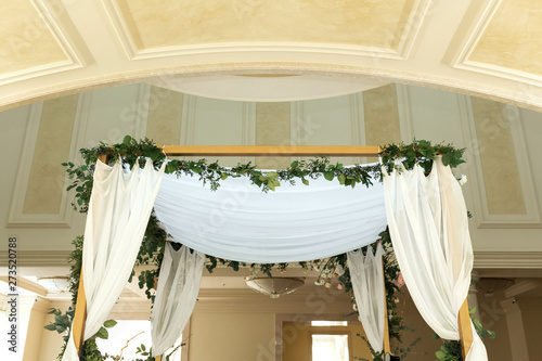 Beautiful wedding huppah decorated with fresh fresh flowers from hydrangea and eucalyptus sheets in a large beautiful wedding hall with a balcony. Wedding floristry photo