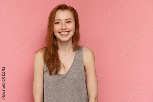 Redhead girl laughs happily looking at the camera and posing over pink background, close-up