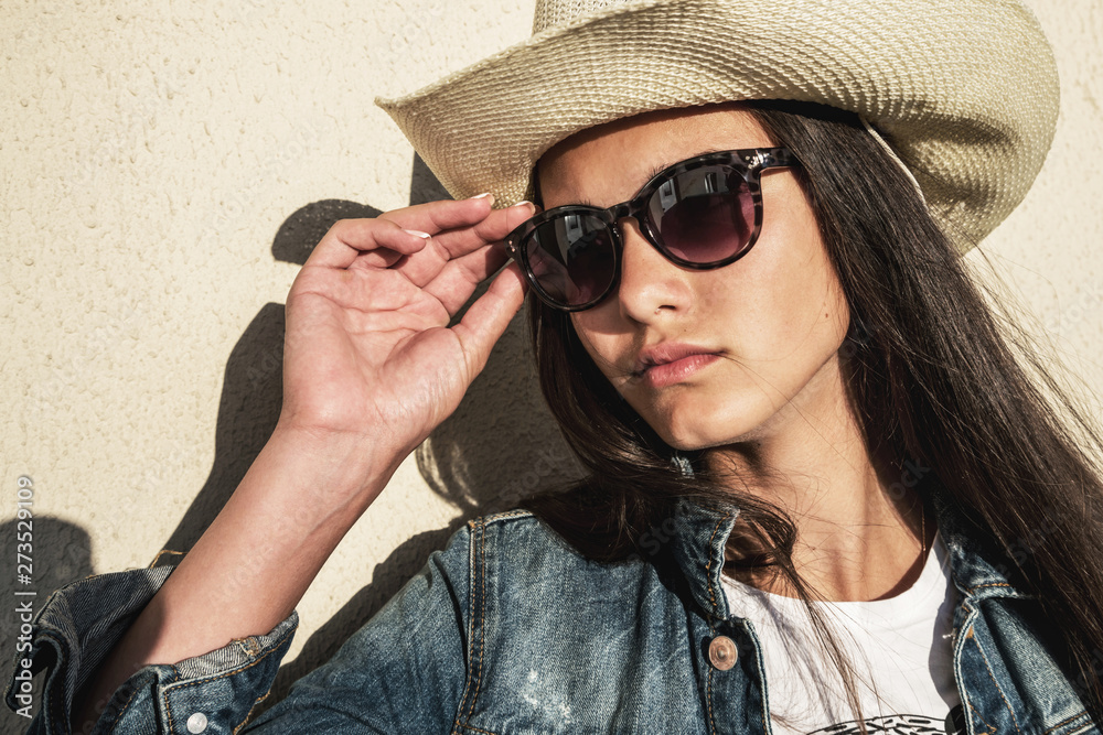 Fototapeta premium young pretty girl posing against background of wall in large hat with brim, jute and sunglasses.