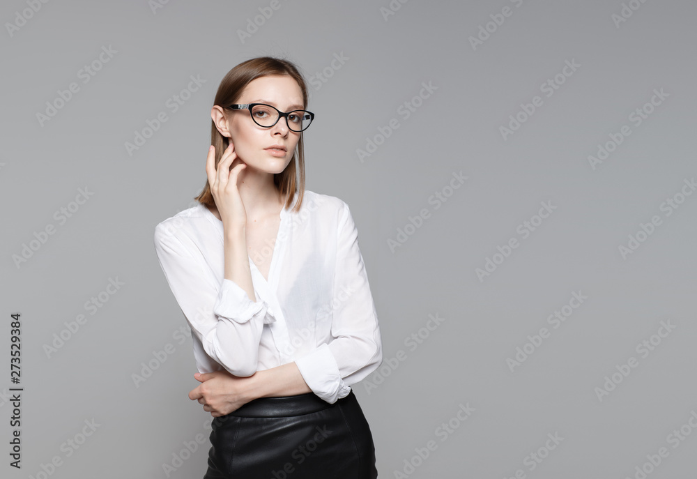 Portrait of the young modern business woman. The strict beautiful thin brunette with the equal business leader of the woman of hair in casual clothes. Gray background. Portrait of the young modern business woman. The strict beautiful thin brunette with the equal business leader of the woman of hair in casual clothes. Gray background.
