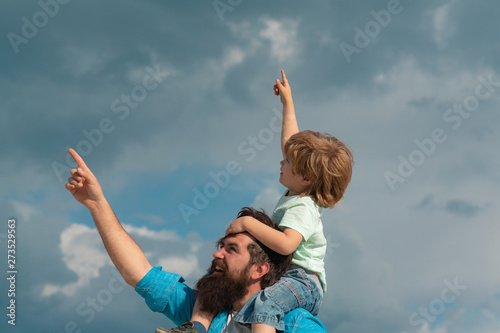 Fathers day. Cute boy with dad playing outdoor. Happy child pointing on summer sky background.