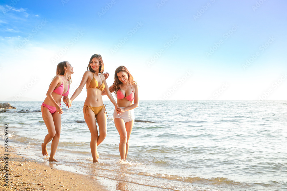 Three Asian women wearing bikinis, playing the sea at the beach