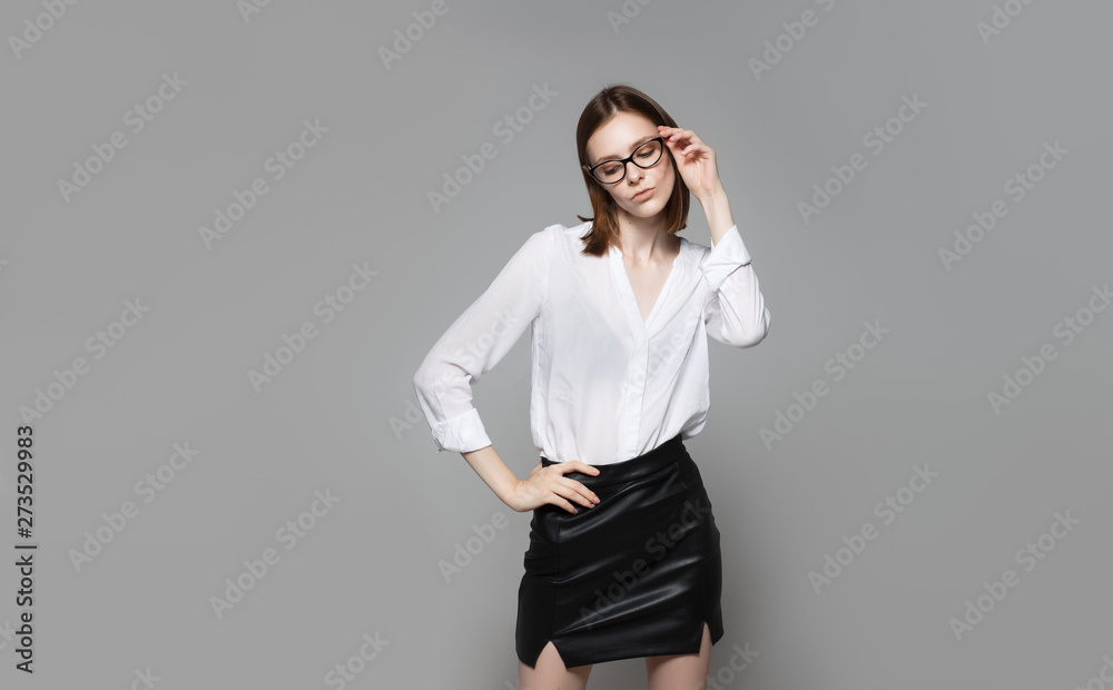 Portrait of the young modern business woman. The strict beautiful thin brunette with the equal business leader of the woman of hair in casual clothes. Gray background. Portrait of the young modern business woman. The strict beautiful thin brunette with the equal business leader of the woman of hair in casual clothes. Gray background.