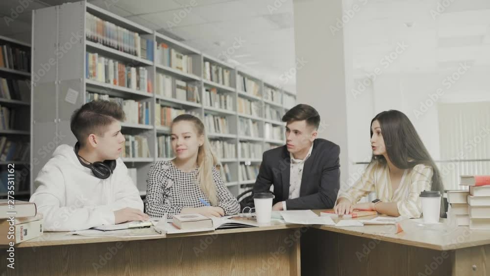Two men and two women college students laughing while preparing for exams while sitting at table at university library Two men and two women college students laughing while preparing for exams while sitting at table at university library