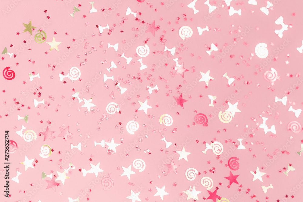 Golden stars flutes and swirls glitter and assorted sparkling confetti partially blurred on trendy pink background. Festive holiday pastel backdrop.