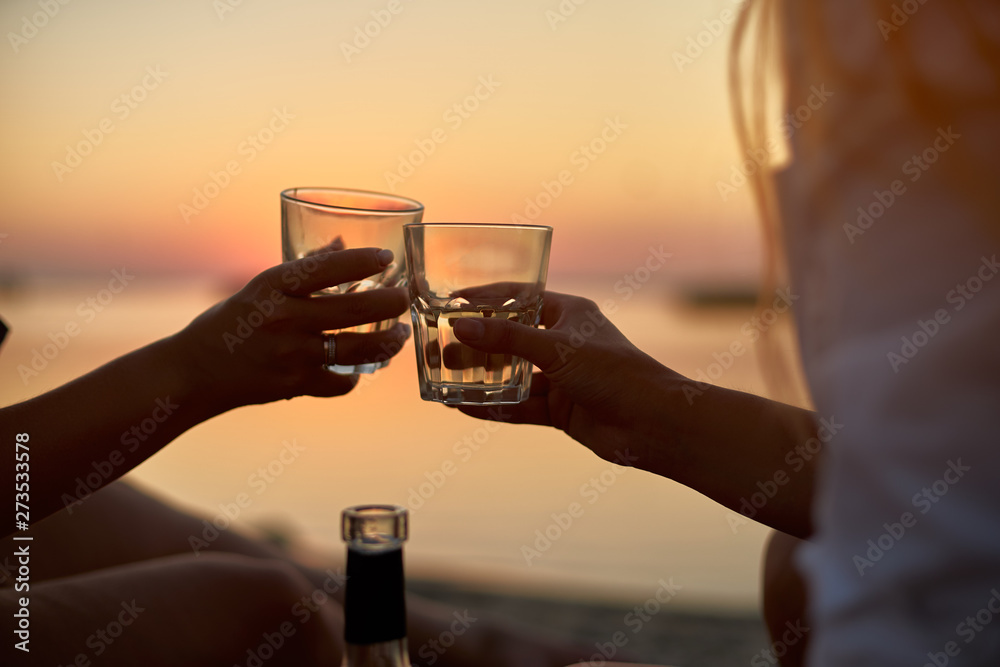 Women clink glasses with white wine on the beach. Girlfriends cheerfully celebrate vacation and proclaim toast on tropical island. Romantic picnic with alcoholic drink beverage near sea on sunset. Women clink glasses with white wine on the beach. Girlfriends cheerfully celebrate vacation and proclaim toast on tropical island. Romantic picnic with alcoholic drink beverage near sea on sunset.