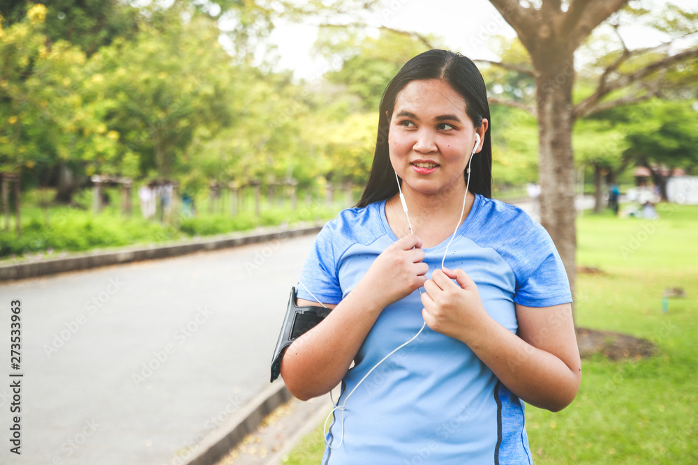 Fat woman, wearing headphones, music, walking, exercising in the park Fat woman, wearing headphones, music, walking, exercising in the park