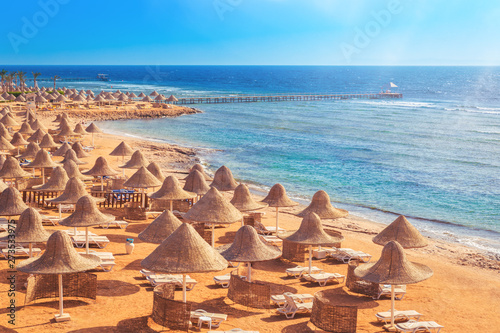 Sandy beach coast line with straw parasols umbrellas and blue sea. Travel destination for vacation concept. Sharm el Sheikh Egypt morning light with copy space photo