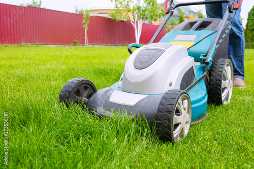 A lawn mower, a close-up. A worker is cutting grass in the backyard on a sunny day.