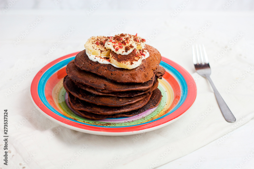 gluten-free chocolate pancakes, proper diet vegetarian food for breakfast with cocoa, Greek yogurt and banana on a colorful rainbow colored plate of LGBT flag colors. LGBT breakfast concept on white 