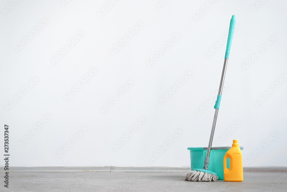Φωτογραφία Bucket with a mop and bottle of detergent on a floor on a white wall background with copy space