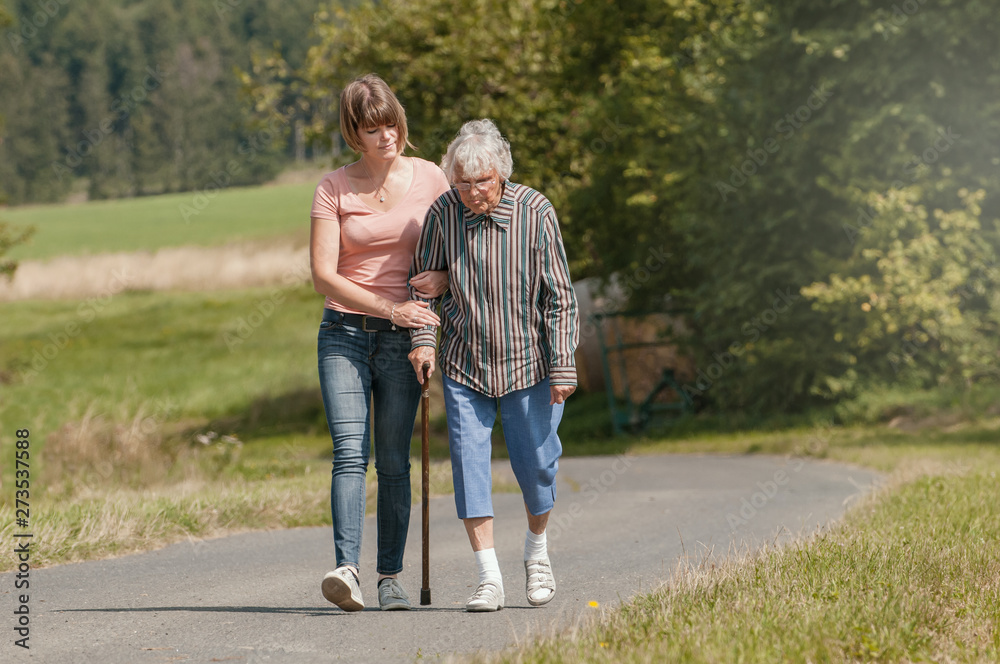 Young woman helps senior woman walking with stick Young woman helps senior woman walking with stick