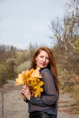 Portrait of young redhead woman with bouquet of yellow leaves
