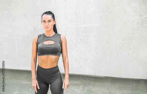 Portrait of a sporty young woman in stylish leggings. Stylish fitness girl on gray background of city streets. 