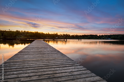 Fototapeta Naklejka Na Ścianę i Meble -  Wooden pier stretching into the lake on a background of dawn. Horizontal frame
