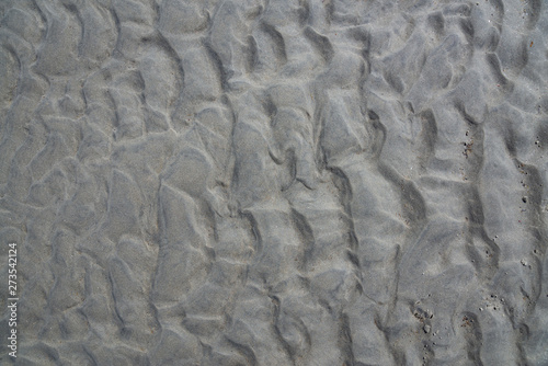 Dark sand on beach with traces of water. Sand on the river. Traces of waves hollowed out in sand on beach