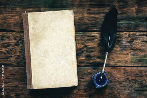 Book, inkwell and a quill pen on a wooden table background with copy space. photo