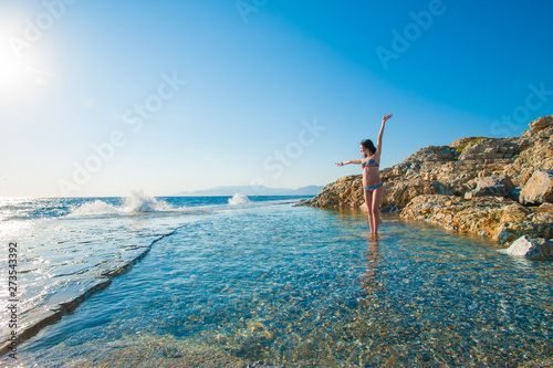 A girl in a swimsuit, splashing from the waves, Brunette girl rejoices splashing from the waves. Young happy woman jumping with raised arms, waving a blue bikini swimsuit in a blue swimsuit and a