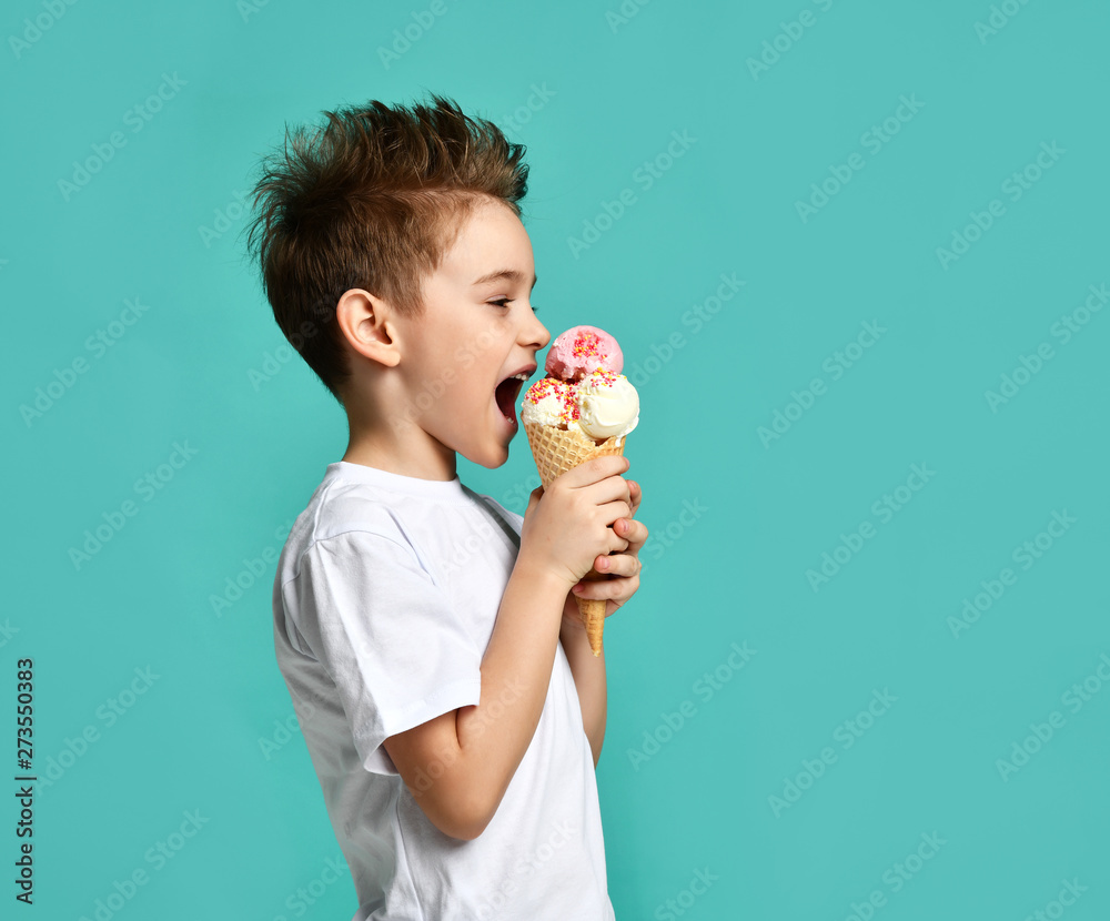 Baby boy kid eat raspberry and vanilla ice cream in waffles cone on blue mint Baby boy kid eat raspberry and vanilla ice cream in waffles cone on blue mint