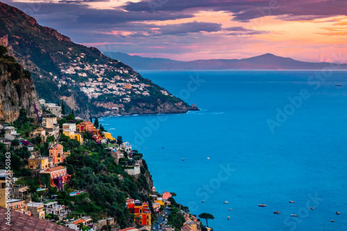 Panoramic sunset view of the Amalfi Coast of southern Italy, including colorful buildings of Positano in the foreground as well as Praiano in distance. 