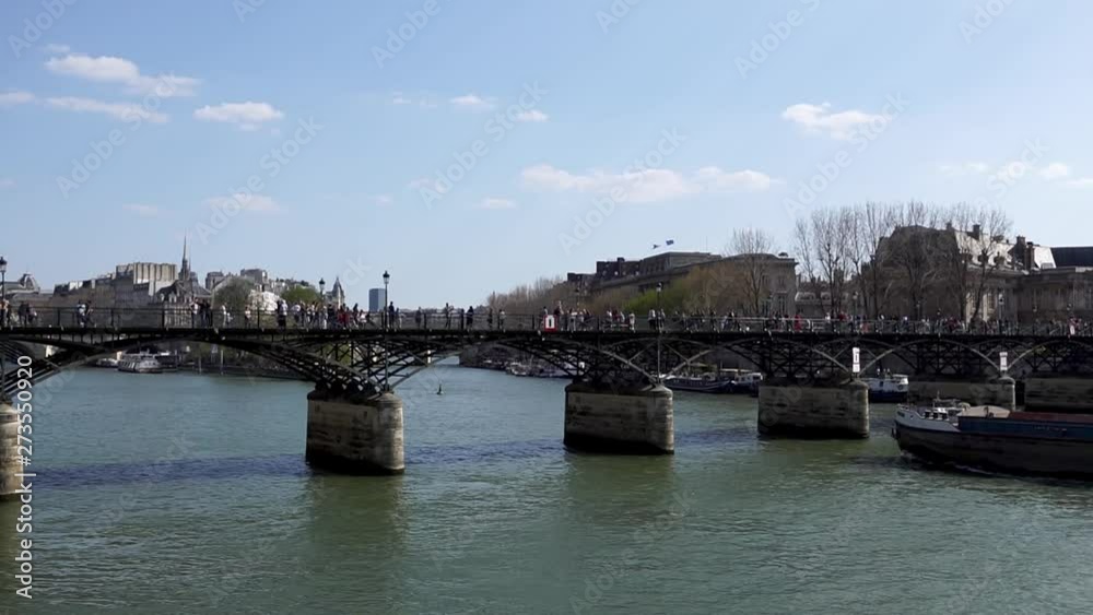 People walking on Pont des Arts bridge on the Seine river with barge traffic and Ile de la Cite in background - Paris, France People walking on Pont des Arts bridge on the Seine river with barge traffic and Ile de la Cite in background - Paris, France