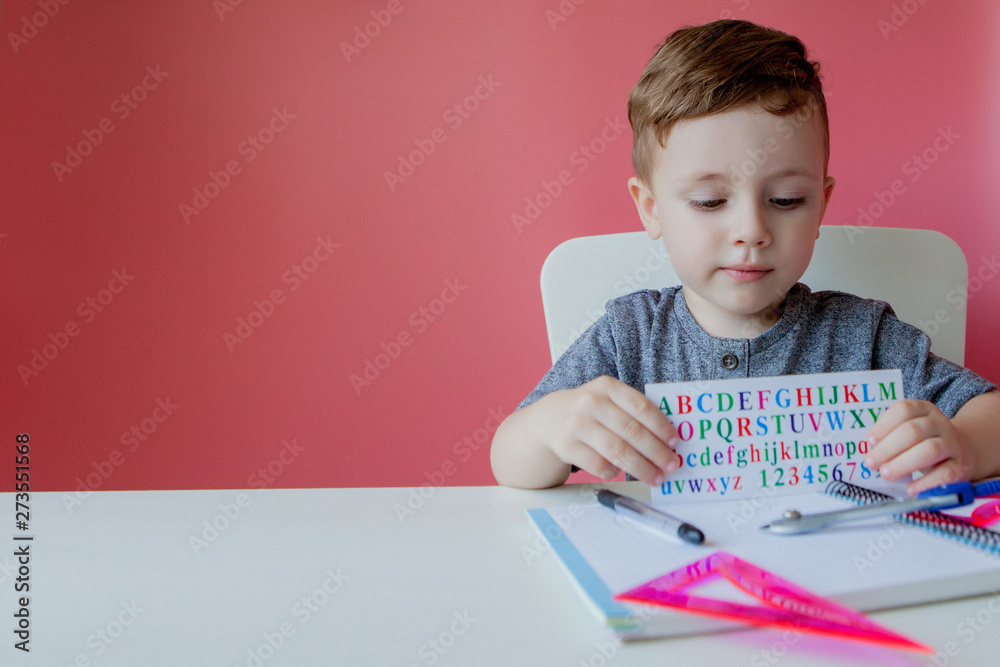 Portrait of cute kid boy at home making homework. Little concentrated child writing with colorful pencil, indoors. Elementary school and education. Kid learning writing letters and numbers Portrait of cute kid boy at home making homework. Little concentrated child writing with colorful pencil, indoors. Elementary school and education. Kid learning writing letters and numbers