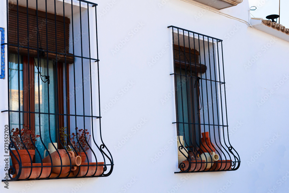 Clay pots on the window behind a forged grid on a white wall in the old city of Altea, Spain