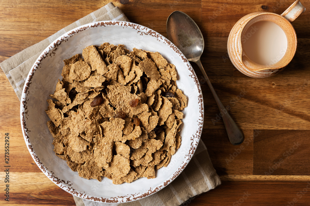 Breakfast bowl of wheat bran flakes and dried sultanas beside a jug of milk. Breakfast bowl of wheat bran flakes and dried sultanas beside a jug of milk.