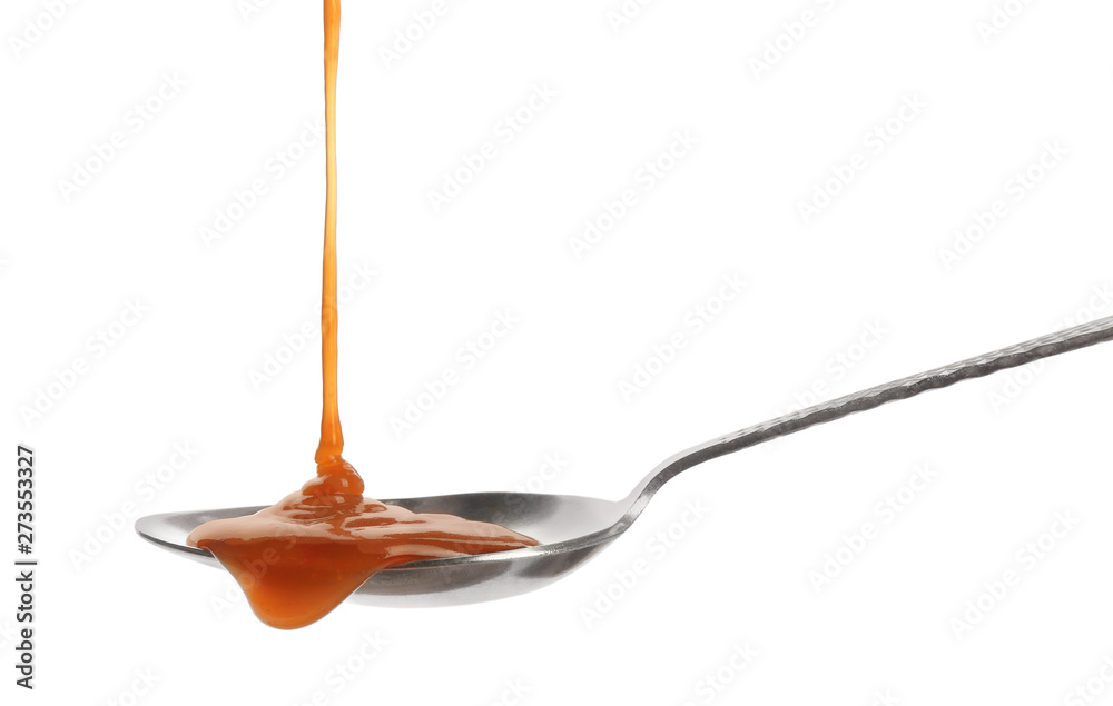 Tasty caramel sauce pouring into spoon isolated on white Tasty caramel sauce pouring into spoon isolated on white