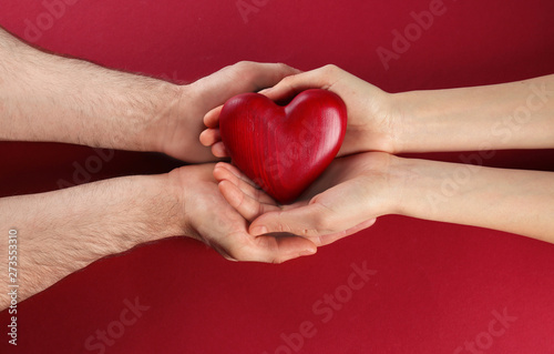 Couple holding decorative heart on color background  top view