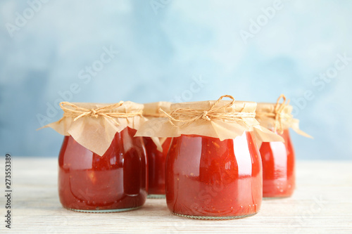 Jars of tomato sauce on wooden table against color background, space for text