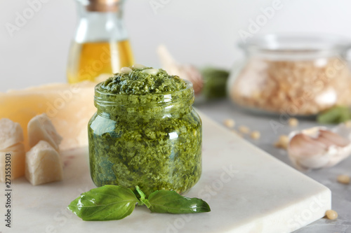 Board with jar of pesto sauce and basil on table. Space for text