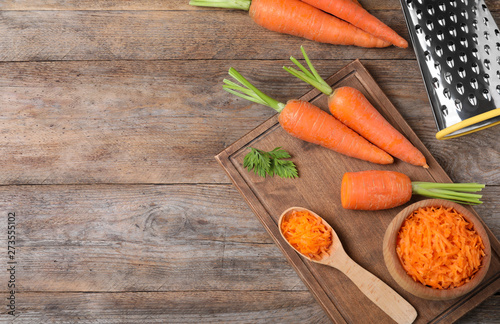 Board with fresh and grated carrots on wooden table, flat lay. Space for text