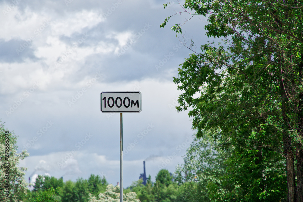 1000m - road sign indicating the distance against the sky, clouds, green foliage and a large plant