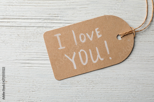 Tag with words I LOVE YOU on wooden background, top view
