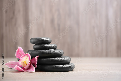 Stack of black spa stones with flower on wooden background. Space for text