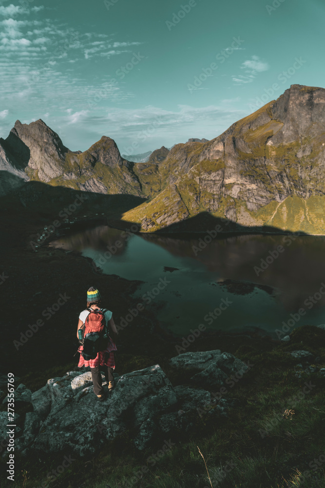 Woman mountaineer standing on rock of peak mountain at sunset. Ryten Mountain, Norway