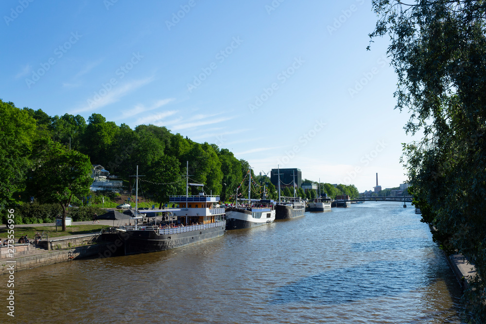 Old vintage ships - restaurants on the Auraioki River and panorama of the city of Turku in Finland on a summer day.
