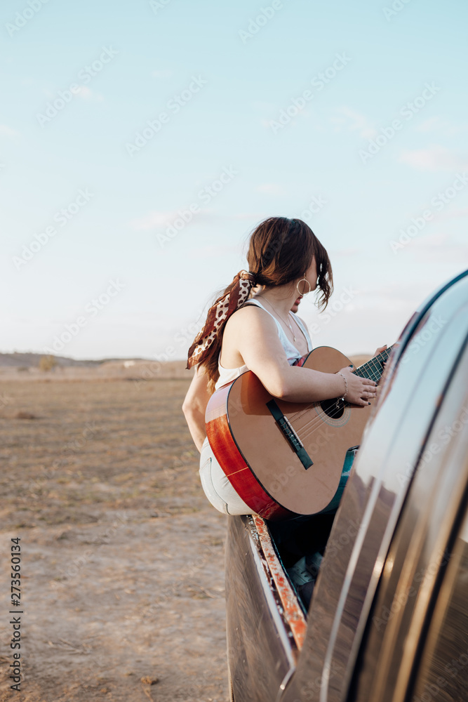 Young traveler woman having fun playing the guitar on top of jeep 4x4 car.  Couple making a wanderlust vacation on sunset at summer Photos | Adobe Stock