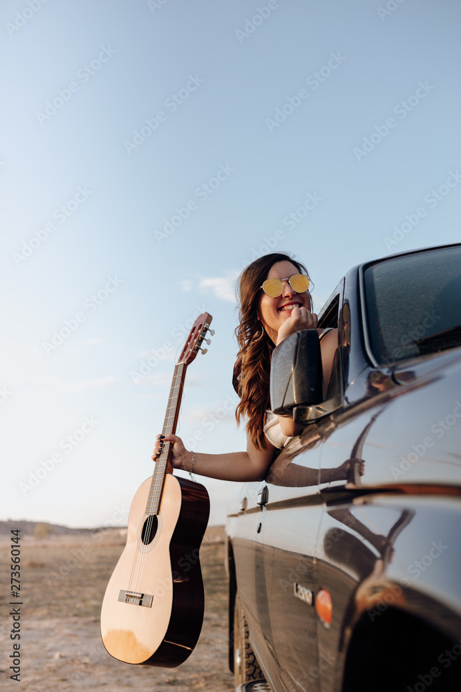 Young traveler woman having fun with the guitar in the jeep 4x4 car making a wanderlust vacation at sunset