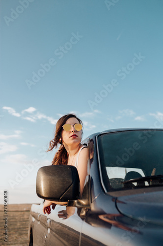 Young traveler woman with sunglasses in the jeep 4x4 car making a wanderlust vacation at sunset © EGHStock