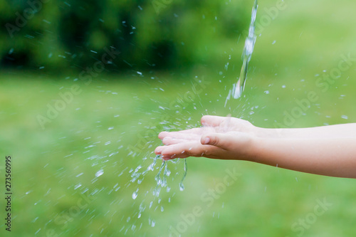 happy little girl catches a jet of water with her hands. child washing hand outdoors. Water pouring in kid hand on nature background, environment issues