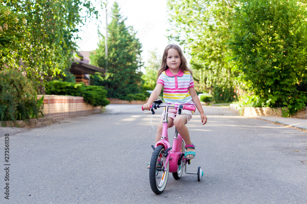 Children ride a bike near the house.  A little girl on a Bicycle on a Sunny summer day. Active healthy outdoor sports for young children. Fun activity for the baby concept